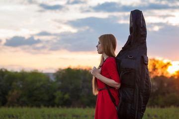 Woman in red dress travelling with cello outdoors © Andrey Milkin