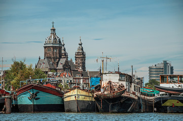 Fototapeta premium Port with rusty moored ships, church towers and building on canal under a sunny blue sky in Amsterdam. Famous for its huge cultural activity, graceful canals and bridges. Northern Netherlands.