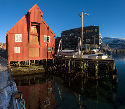 Red wooden boathouse in the docks of the harbor of Tromsø on a sunny morning, Tromsø, Norway