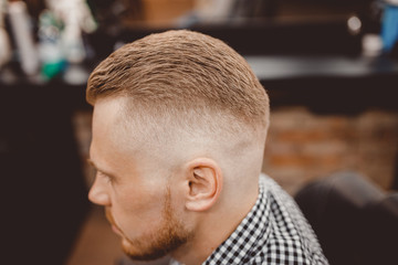 Obraz premium Man in barber chair, hairdresser styling in barbershop. close-up for parting and transition