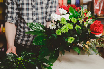 Workplace florist, man collects modern bouquet of hands of roses and white chrysanthemums