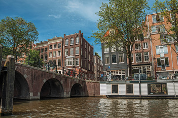 Fototapeta na wymiar Bridge with bicycles, moored boats, old brick buildings and sunny blue sky in Amsterdam. The city is famous for its huge cultural activity, graceful canals and bridges. Northern Netherlands.