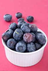Delicious ripe blueberries on white bowl against bright raspberry background