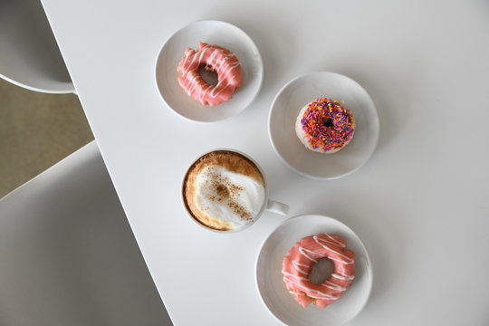 Coffee and pink glazed donuts on table