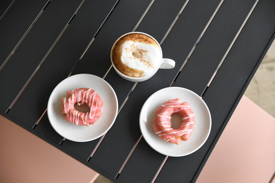 Coffee and pink glazed donuts on plates