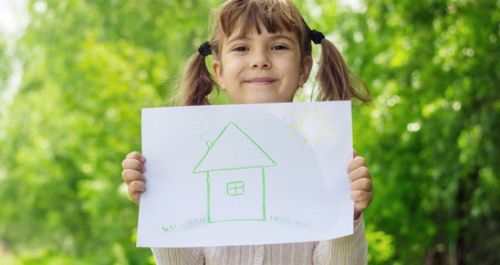 Drawing of a green house in the hands of a child. Selective focus.