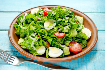 Dietary food green salad with tomatoes, cucumber and quail eggs in a clay plate