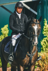 Showjumping competition, bay horse and rider in black uniform going performing jump. Equestrian...