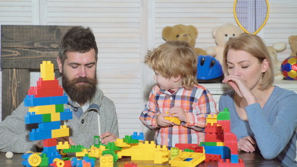 Young family in playroom. Love family concept. Mom, dad and boy with toys build out of plastic blocks. Parents and son smiling, make brick constructions.