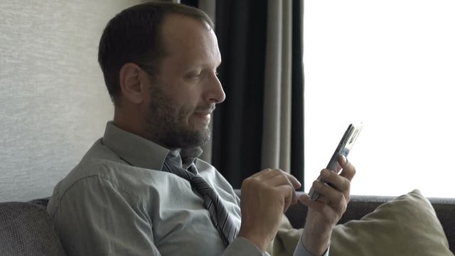Young businessman texting on smartphone sitting on sofa at home
