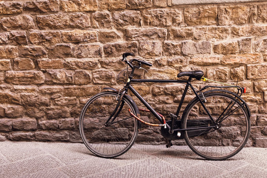 Black old bicycle against stone wall with copy space, toned.
