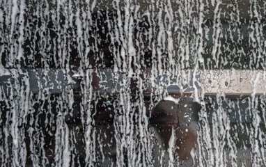 Car wash foam flowing down on shiny window to body part