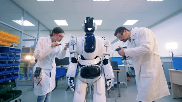 Male and female technicians are performing a maintenance procedure on a robot