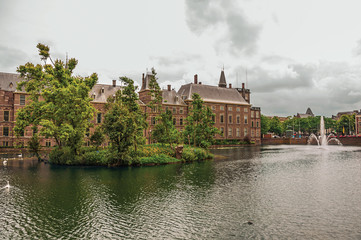 Green isle on the Hofvijver lake with the Binnenhof (Gothic government buildings) and cloudy sky in The Hague. Important political center, is a mix of historic city with modernity. Western Netherlands