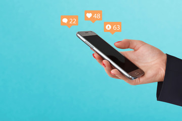 Female hand holding phone, surrounded with social media icons on blue background. Social media...