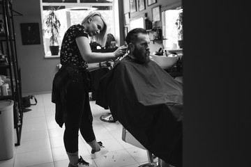 Stylish hairdresser cutting hair of client at barber shop. Beard man getting haircut at salon.