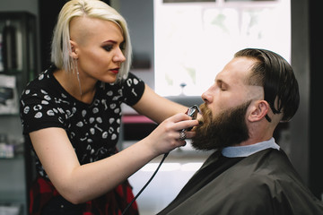Fototapeta premium Getting perfect shape. Close-up side view of young bearded man getting beard haircut by hairdresser at barbershop