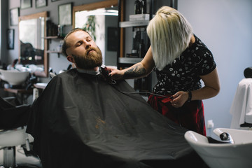 Getting perfect shape. Close-up side view of young bearded man getting beard haircut by hairdresser at barbershop