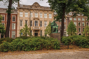 Fototapeta na wymiar Bronze statue, garden with leafy trees in front of brick buildings and cloudy sky in The Hague. Important political center, is a mix of historic city with modernity. Western Netherlands.