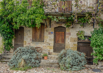 Fototapeta na wymiar Najac, Midi Pyrenees, France - September 16, 2017: Old stone facade with several wooden doors surrounded by vines and plants