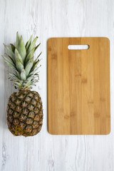 Large ripe pineapple with bamboo cutting board. White wooden background, top view. From above.  Flat lay. Copy space.