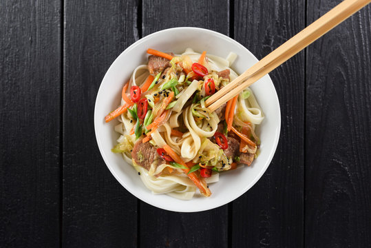 Traditional Asian noodles minimalist style. Stir fry udon noodles with meat, vegetables, chili and spring onion on black background top view