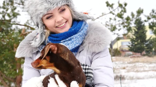 Young woman playing with her little puppy dog outdoor during winter weather.