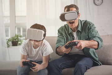 Cheerful family enjoying video game competition. They are holding joysticks and wearing virtual...