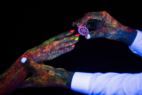 concept of connecting hands creative wedding photography in neon light male and female palms together hold on to each other the guy makes an offer with an engagement ring and the paint on them glow in