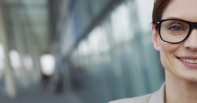 Close up of the half face in glasses of the pretty smiled Caucasian businesswoman on the blurred background of the office building