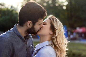 Fototapeta premium Young cute couple is kissing on the park background on a beautiful sunny summer day, close-up.