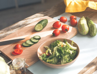 Close up of bowl with fresh salad on table in kitchen. Chopped cucumber with tomato on wooden board