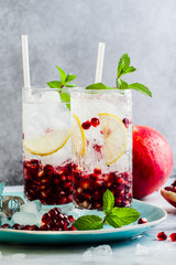 refreshing alcoholic drink with lemon and pomegranate seeds on a white stone table and gray...