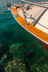 Obraz premium Hidden Danger - Bow Tip of a private Yacht, green, crystal-clear Water, with dangerous Rocks below the Surface in the Ocean