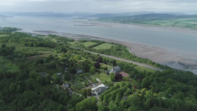 Aerial footage over woodland to a large country house and gardens near the village of Langbank on the south shore of the Firth of Clyde with view to hills in the distance.