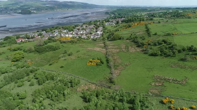 Aerial footage flying over woodland and yellow gorse covered hillside to the village of Langbank on the south shore of the Firth of Clyde.