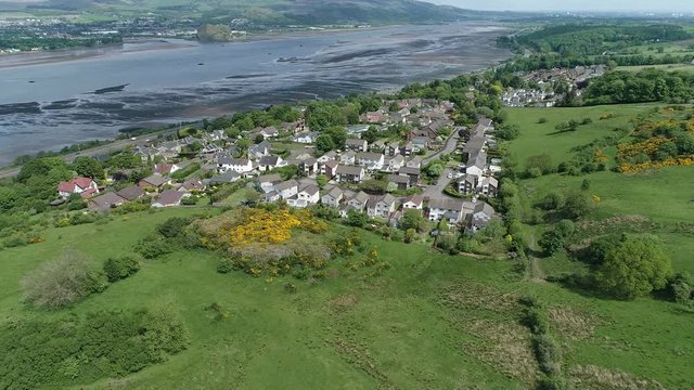 Aerial footage over woodland and yellow gorse covered hillside to the village of Langbank on the south shore of the Firth of Clyde.