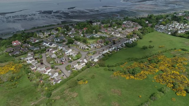 Aerial footage of the village of Langbank on the south shore of the Firth of Clyde flying to the right over woodland and yellow gorse covered hillside.