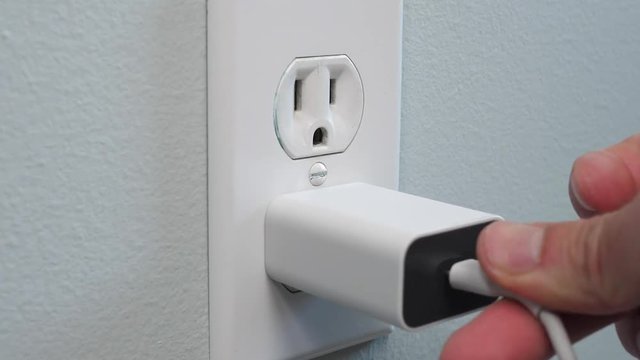 Plugging the smartphone power charger into a outlet wall socket.