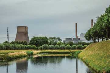 View of canal and gardens with nuclear power plant in background on cloudy day, near the village of...