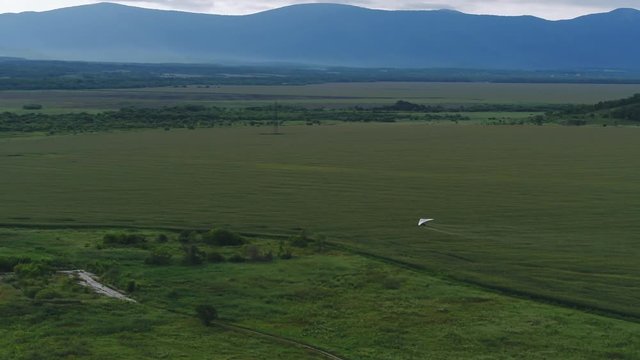 AERIAL VIEW from above of a flying paraglider. Beautiful paraplaner on the background of wild nature: rocky mountains, green meadows and plains 4k
