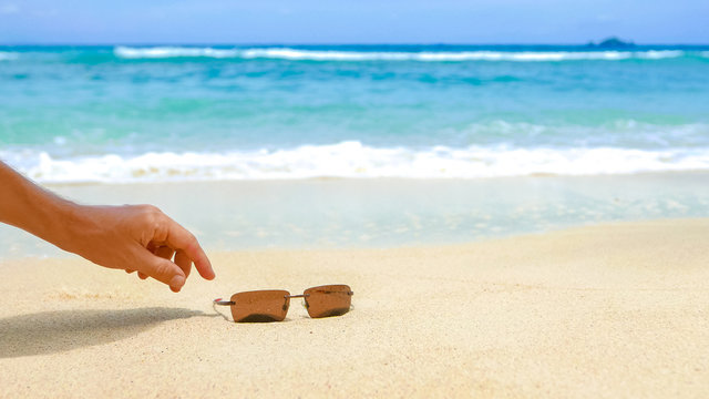 Summer sale vacation background, person points the sunglasses on pristine tropical beach