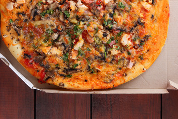 Pizza in a box on a wooden background. Italian pizza with chicken, mushrooms, greens, cheese and sauce. Festive meal in a cardboard box