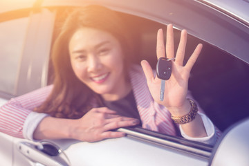 Asian driver woman smiling and showing new car key while sitting in a car that she taking it from...