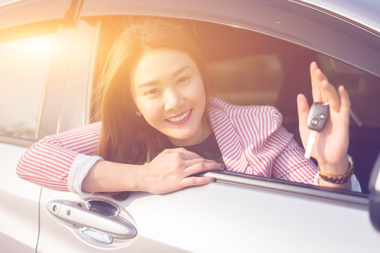 Asian driver woman smiling and showing new car key while sitting in a car that she taking it from dealer in the auto show. transport business, car sale for consumerism and people concept,vintage color