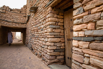 White dressed Beduin in front of historic bricked houses at world hertiage site Tichitt, Mauritania