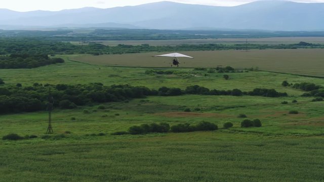 AERIAL VIEW from above of a flying paraglider. Beautiful paraplaner on the background of wild nature: rocky mountains, green meadows and plains 4k