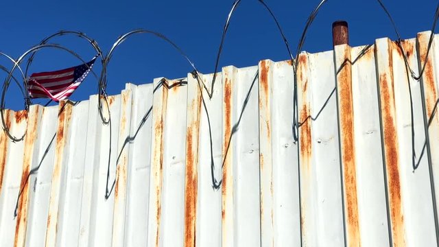 American flag waving behind rusty fence with razor barbed wire
