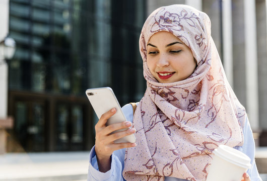 Islamic woman using mobile phone and holding coffee cup