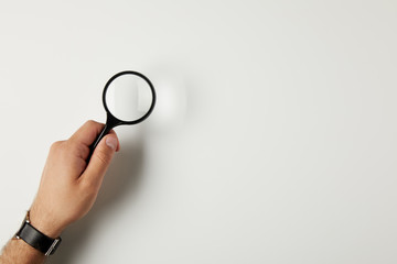 cropped shot of male hand with wristwatch holding magnifying glass on grey